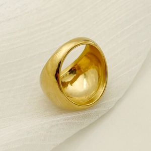 Polished gold plated wide stainless steel ring on minimalist cream fabric background