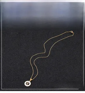 Macro detail of golden necklace showing a round pendant with black letter R on white inlay