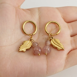 Detailed close-up of gold feather earrings with pink natural stone beads held in hand