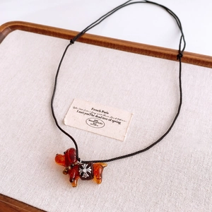 Détail d'un pendentif teckel en verre brun avec anneau de croix fleurie en argent
