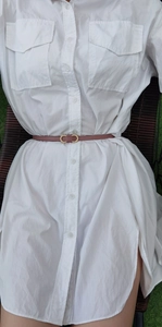 Detail of pink thin leather belt with interlocking gold buckle on white shirt dress