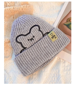 Detail of grey knitted beanie with bear embroidery and yellow label on lace background