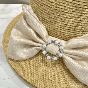 Close-up of straw sun hat featuring a champagne satin bow with a pearl buckle detail