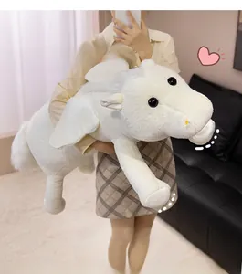 Close-up of a soft white plush Pegasus toy with wings held in a cozy home setting