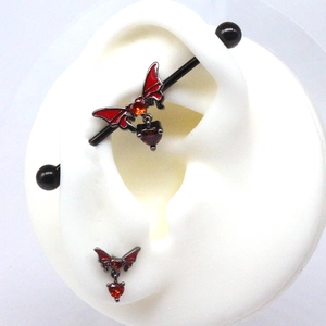 Detail of red bat heart charm industrial barbell on a white silicone ear model