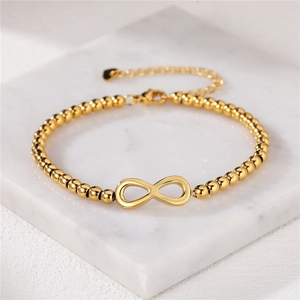 Polished gold infinity symbol bracelet with metal beads on a marble surface