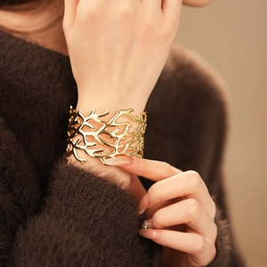 Close-up of a wide gold open cuff bracelet with an intricate organic hollow structure