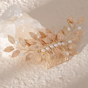 Elegant gold leaf bridal hair comb with white pearls on a minimalist textured background