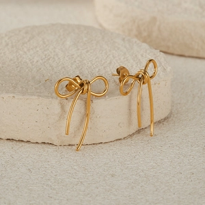 Close-up of golden bow-shaped minimalist earrings on textured beige stone background