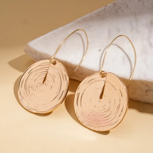 Macro detail of golden round earrings with concentric texture on white marble surface