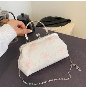 Detailed shot of cream lace evening bag with pink floral embroidery and pearl clasp handle