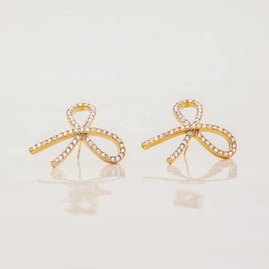 Close-up of 18K gold-plated bow earrings with pavé white rhinestones on a white surface