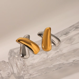 Macro shot of gold and silver X-shaped stainless steel earrings on crystal glass