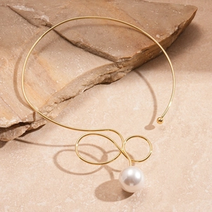 Detail of a minimalist gold collar necklace with a white pearl on a natural stone surface
