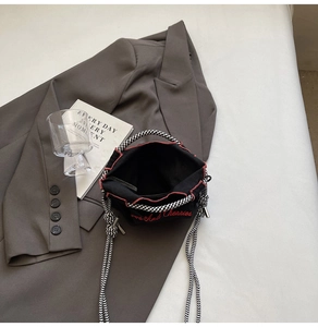 Detail of black nylon bucket bag featuring red floral embroidery and woven check handles