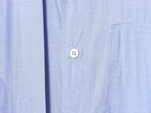 Detailed macro view of light blue shirt fabric texture and white button stitching