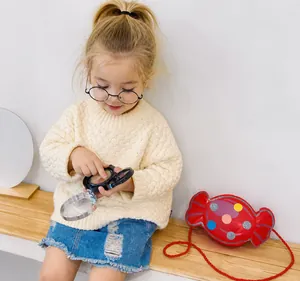 Fillette avec lunettes sur un banc portant un joli sac bandoulière rouge en forme de bonbon