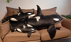 Three sizes of plush orca toys displayed on a sofa showing the size gradient