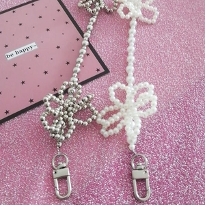 Beaded pearl crossbody bag chain with silver bow and metal hooks on pink glitter background