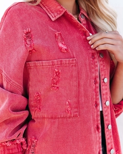 Close-up of red distressed denim jacket featuring metal buttons and frayed rip details