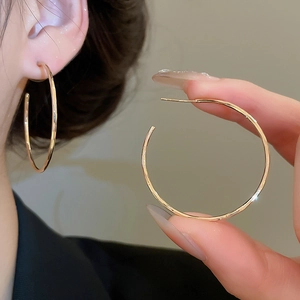 Gros plan d'un mannequin portant de grandes créoles dorées minimalistes en métal de haute qualité