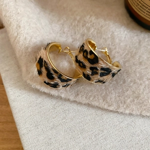 Detailed view of leopard print faux fur C-shaped earrings on a soft grey felt background