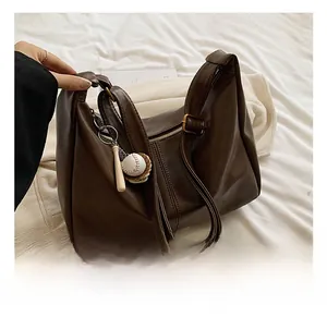 Close-up of dark brown matte leather tote bag with miniature baseball charms on white knit