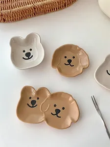 Close-up of cute bear and dog ceramic sauce dishes in cream and brown on a white table