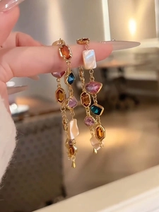 Detail of colorful faceted gemstones and white shell inlays on golden drop earrings
