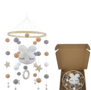 Detail of wooden baby mobile with plush bunny and felt balls next to its retail box