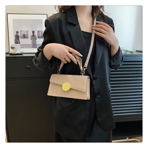 Détail d'un sac à main beige carré avec fermoir magnétique doré et poignée plissée