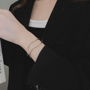 Detail of silver wavy open cuff bracelet on a model wearing a black blazer jacket