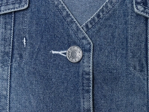Gros plan détaillé sur le denim bleu délavé avec un bouton métallique argenté vintage