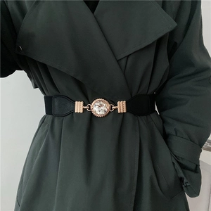 Detail of a black elastic belt with a gold buckle and large crystal on a green coat