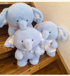 Three light blue plush elephants in varied sizes arranged on wooden stairs