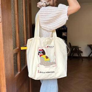 Detail of beige canvas tote bag featuring cute cartoon dog embroidery and drawstring closure