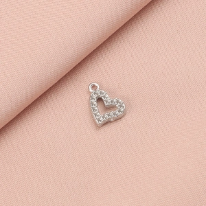 Detailed view of a silver heart-shaped pendant with a textured beaded border on pink cloth