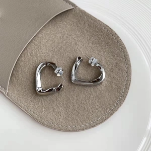 Minimalist silver geometric twist heart earrings on a premium grey suede jewelry pouch