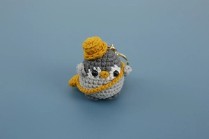 Close-up of handmade crochet penguin keychain with yellow hat and scarf detailing