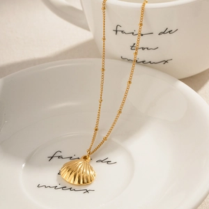 Close-up of a gold shell pendant on a fine chain resting on a white ceramic saucer