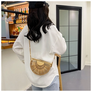 Detail of a semi-circular woven bamboo bag with beaded strap on a female model