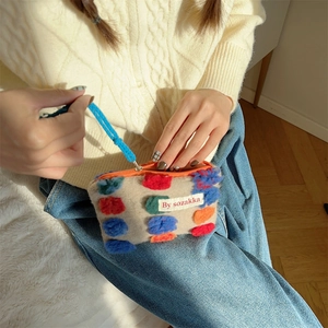 Dettaglio della pochette in peluche con pompon colorati e cordino blu per cerniera