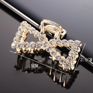 Macro shot of a 5x2.5cm gold hair claw clip with white rhinestones on black reflection