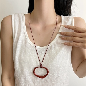 Minimalist red geometric irregular pendant on a matching cord shown on a model