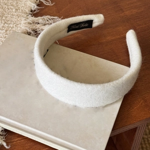 Dettaglio del cerchietto in peluche beige con etichetta Hand Made su scrivania