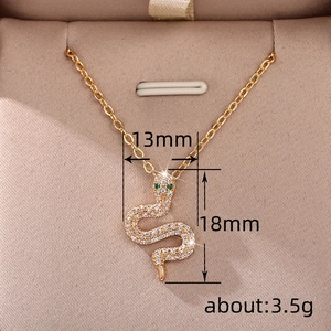 Gold snake pendant necklace with white cubic zirconia and green gem eyes on velvet box