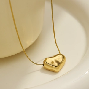 Close-up of a polished gold heart pendant with a fine snake chain on a ceramic plate