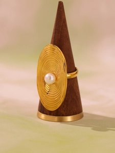 Detail of gold oval ring with white pearl on concentric wave textured stainless steel band