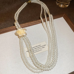 Close-up of multi-layer pearl necklace featuring a diamond-encrusted yellow rose pendant
