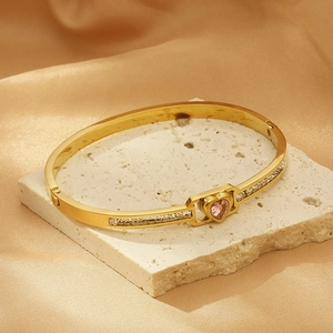 Detail of a gold heart bracelet with a pink gem and white pavé crystals on stone